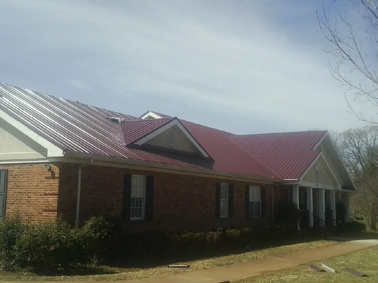 Red metal roof with gabled entries on a long brick building, from a Hail Damage Roof Repair job in Abita Springs