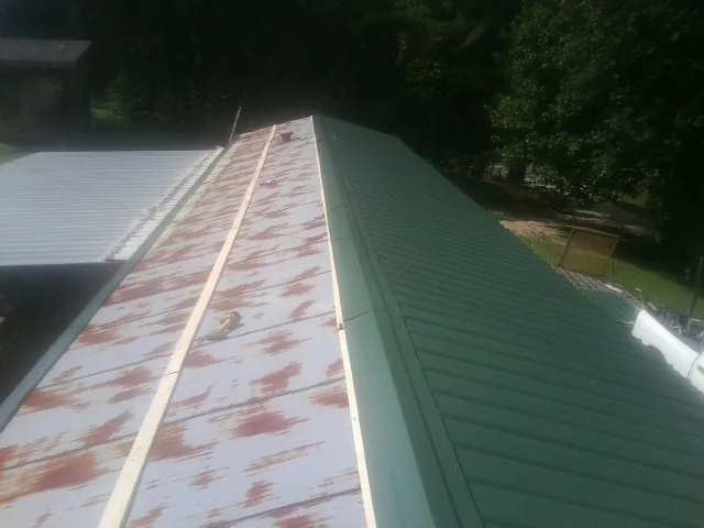 Old rusted panels beside newly installed green metal roofing — Wind Damage Roof Repair by Roofing Brothers in Abita Springs