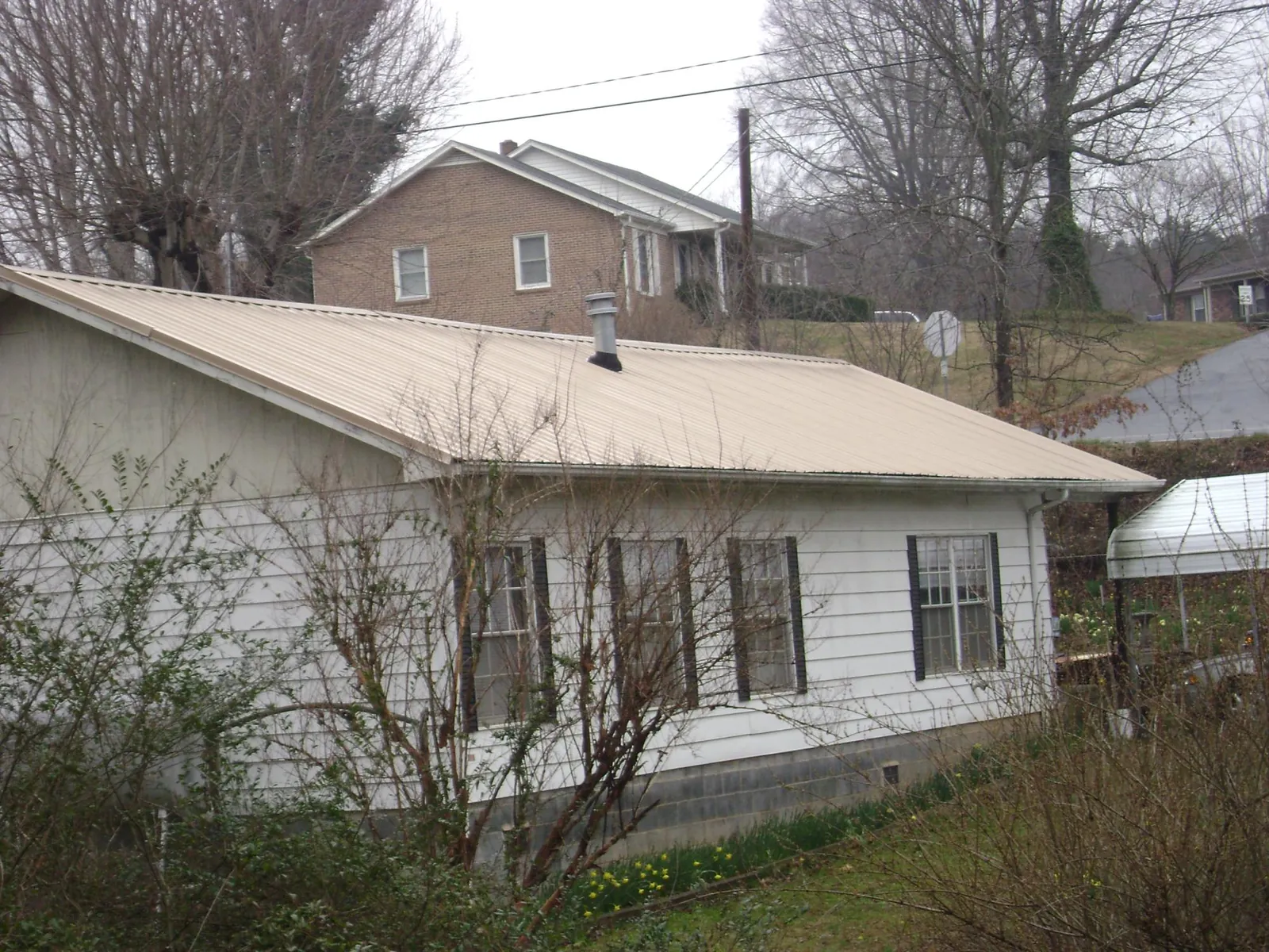 Tan metal roof on a white sided house set into a hillside — Commercial Roofing by Roofing Brothers in Abita Springs