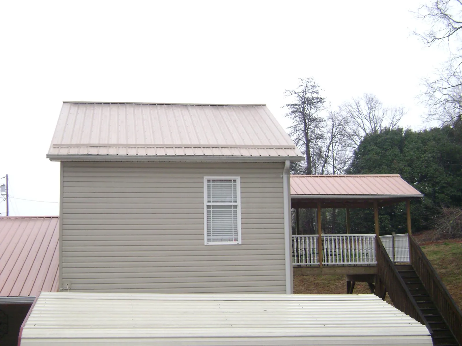Tan metal roofs on a two story addition and attached porch, from a Roof Replacement job in Abita Springs